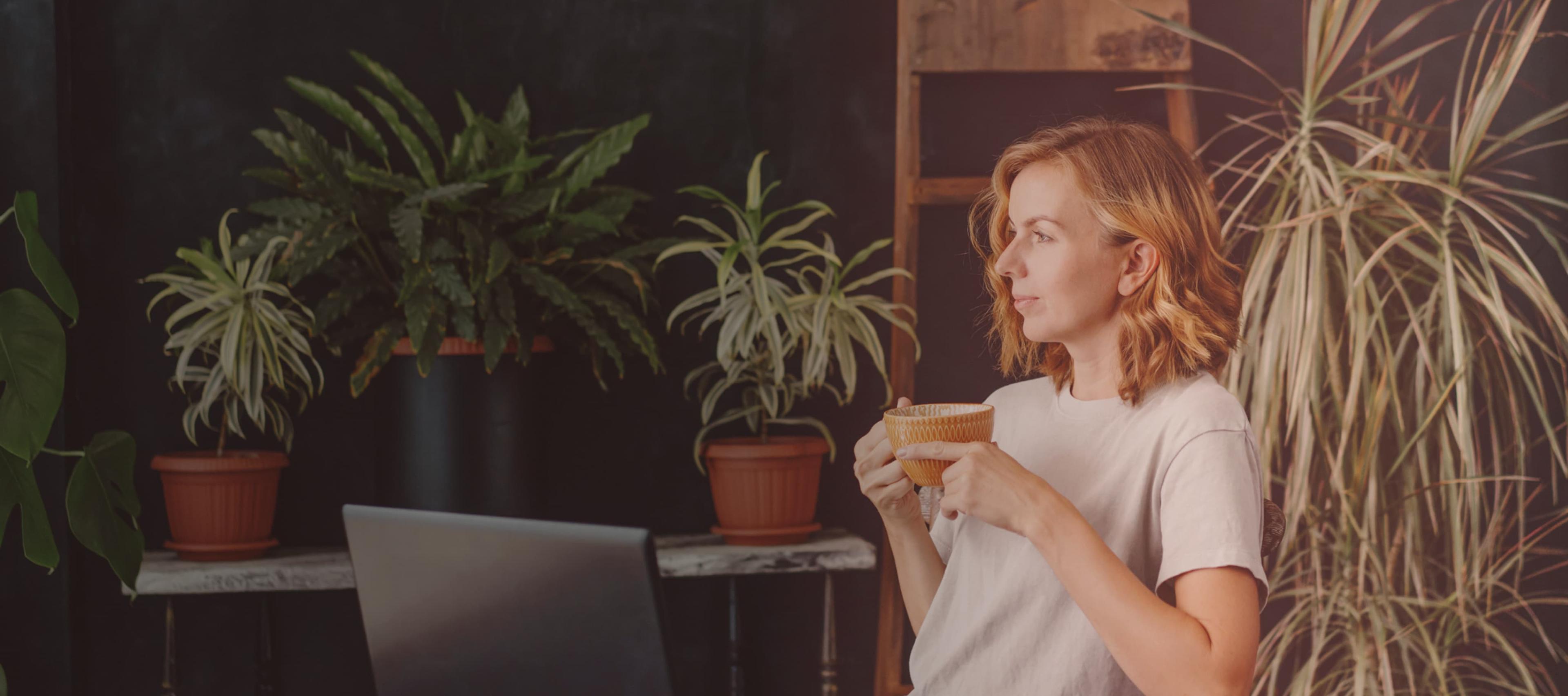A woman drinks coffee in front of a laptop